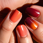 **Prompt:** Close-up of hands with warm-toned coral and orange nail polish shades, one hand showcasing a gradient effect, the other with a unique mix of red and brown creating a burgundy color, illuminated by warm natural light.